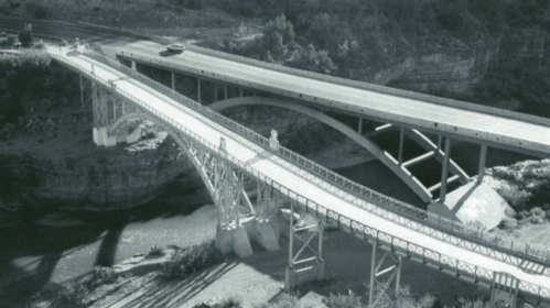 Aerial view of two bridges crossing over a canyon, one modern and one older, surrounded by rocky terrain.